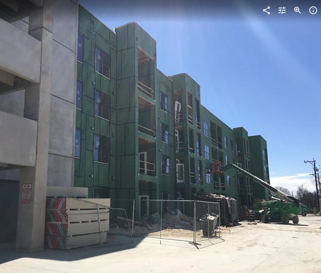Modern multi-story apartment building under construction with green paneling and concrete facade on sunny day